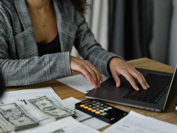 Vrouwelijke handen van budgetcoach, typend op laptop, met een calculator en geld op tafel